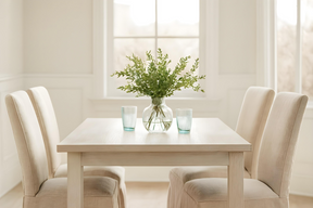 Dining room with a table and chairs, featuring a vase of flowers and glasses.